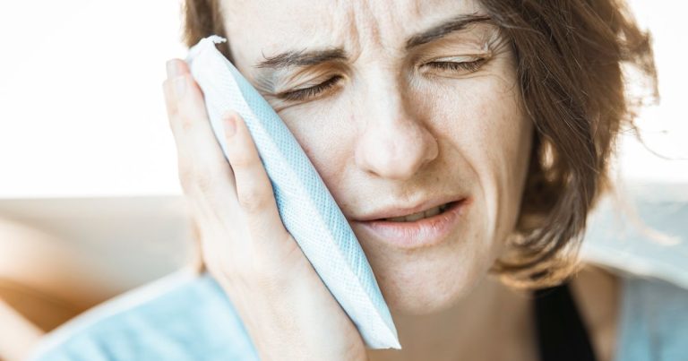 Woman holding a cold compress against her cheek while wincing from jaw pain